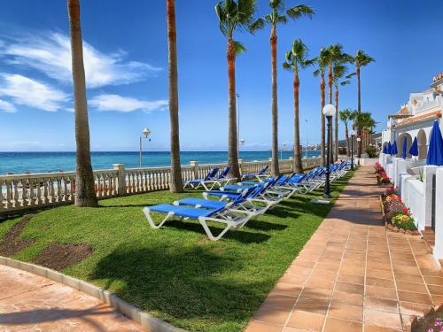a row of blue lounge chairs next to the beach at Apartamentos Perla Marina in Nerja