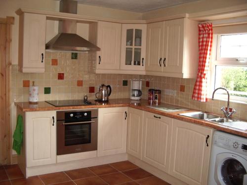 a kitchen with white cabinets and a sink and a stove at Annagh Cottage in Bellaghy