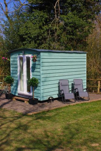 a blue shed with two chairs and a window at Hopgarden Glamping and camping - Luxury furnished Bell tents & Shepherd huts plus camp field to pitch your own tents in Wadhurst