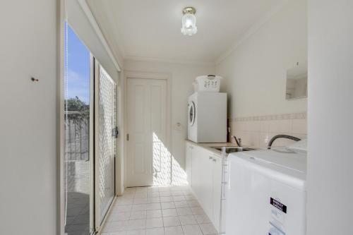 a white kitchen with a refrigerator and a sink at Tondo in Lakes Entrance