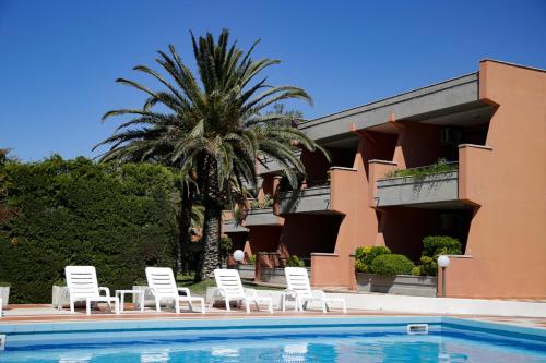 a pool with chairs and a palm tree in front of a building at Appartamenti Maricampo - HelloElba in Marina di Campo