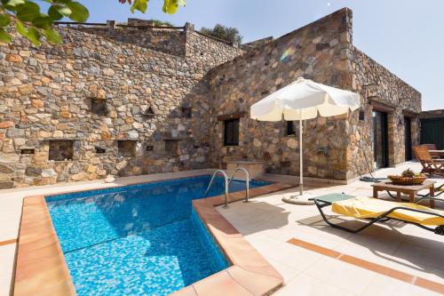 a pool in front of a stone building with an umbrella at Meliti Sunset View & Private Pool Villa 20 min from Elafonissi in Livadia