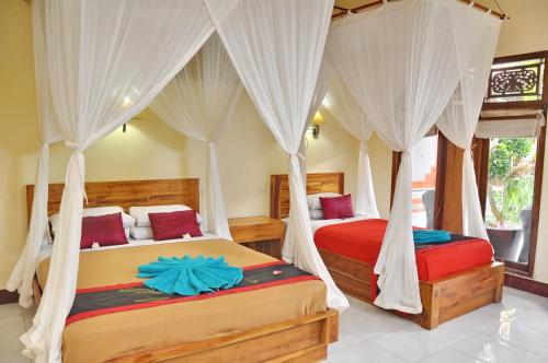 two beds in a bedroom with white drapes at Nick's Homestay in Ubud