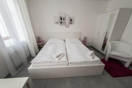 a white bedroom with a white bed and a chair at Rezidence Černý medvěd in Znojmo