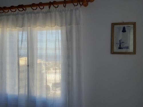 a window with white curtains and a picture on a wall at Katerina Kafieri Apartments in Firostefani