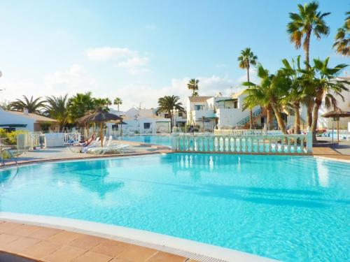 a large swimming pool with palm trees and houses at New central town Bungalow WiFi Netflix in Caleta De Fuste