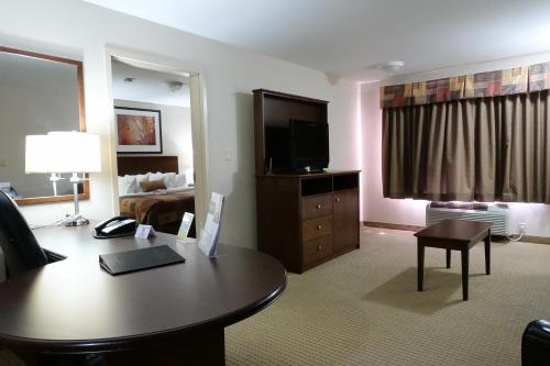 a hotel room with a desk with a television and a bed at Ramada by Wyndham Weyburn in Weyburn