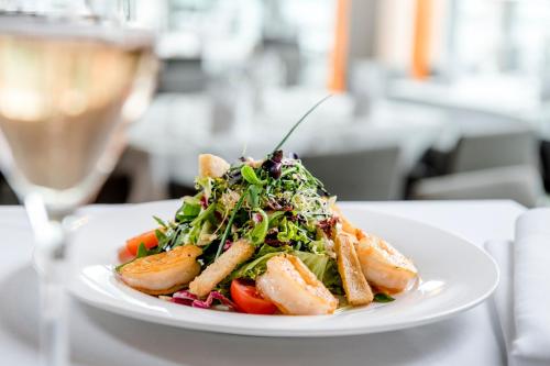 a plate with a salad on a table with a glass of wine at IMLAUER HOTEL PITTER Salzburg in Salzburg