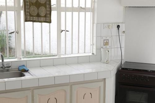 una cocina con armarios blancos, fregadero y ventanas en Le Grand Cacatoie, en Blue Bay