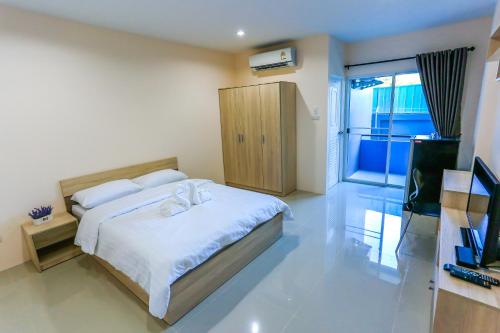 een slaapkamer met een bed met witte lakens en een televisie bij Tempo Plus Apartment in Mae Sot
