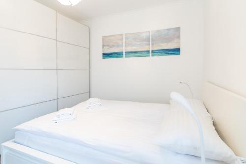 a white bedroom with a bed and a painting at Kolorowe Balkony III by Renters in Międzyzdroje