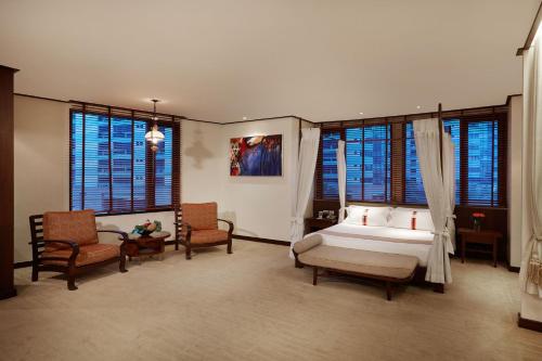 a bedroom with a bed and chairs and windows at The Davis Bangkok in Bangkok