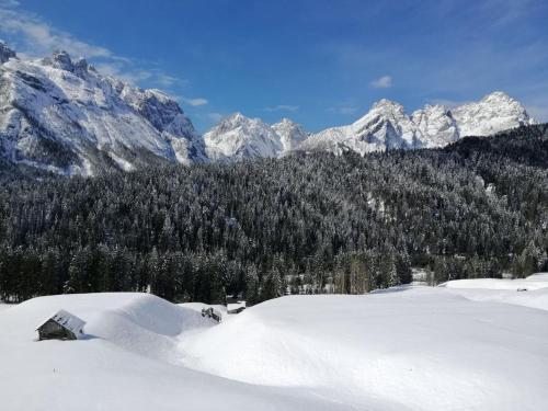 a snow covered mountain range with a house in the foreground at Plodn House in Sappada