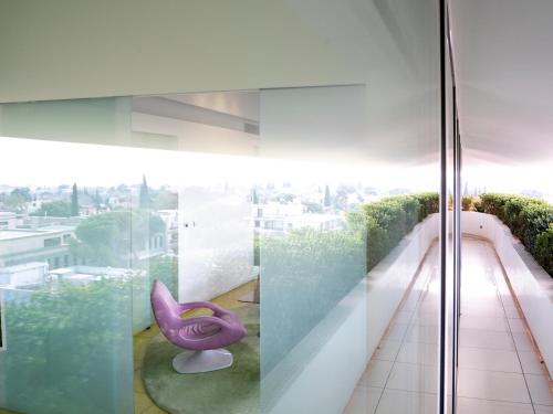 Habitación con paredes de cristal y silla morada en el balcón. en Semiramis en Athens