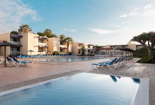 a swimming pool in a resort with blue chairs and buildings at Hotel Palia Don Pedro in Costa Del Silencio