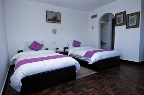 a bedroom with two beds with white sheets and purple pillows at Dhulikhel Mountain Resort in Dhulikhel