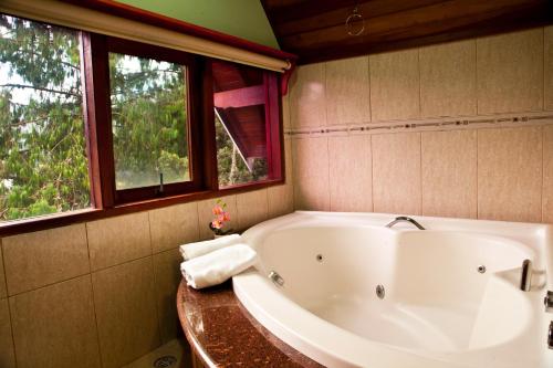 a bath tub in a bathroom with two windows at Pousada Oliveri in Monte Verde