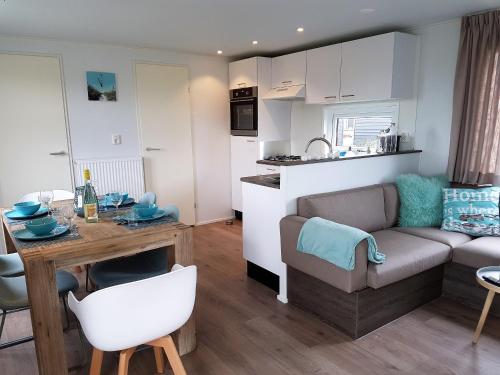 eine Küche und ein Wohnzimmer mit Sofa und Tisch in der Unterkunft Chalet Veere - eingezäunter Garten, hundefreundlich & ruhig in Zeeland in Serooskerke
