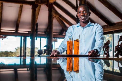 Ein Mann, der einen Tisch mit orangefarbener Flüssigkeit darauf hält. in der Unterkunft Chaminuka Lodge in Lusaka