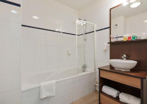 a bathroom with a tub and a sink and a mirror at Zenitude Hôtel-Résidences Béziers Centre in Béziers