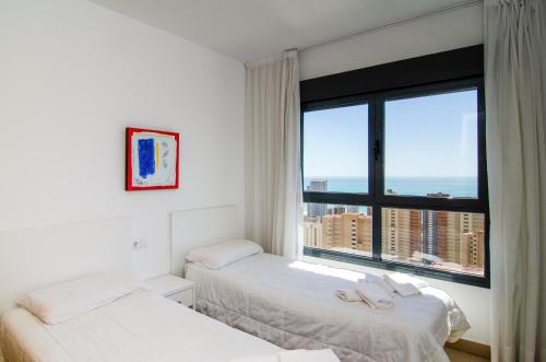 Dos camas en una habitación con una gran ventana. en Apartamentos con terraza Torre D'Oboe by Renthas, en Benidorm