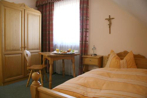 ein Schlafzimmer mit einem Bett und einem Tisch mit einem Kreuz am Fenster in der Unterkunft Landgasthof Stangl in Moosinning