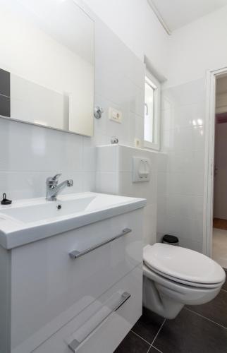 a white bathroom with a toilet and a sink at Apartments Luka in Pag