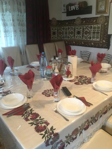 una mesa con platos blancos y flores rojas. en Casa Ionela Petreus en Poienile Izei