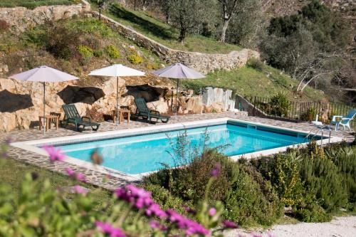 a swimming pool with two umbrellas and chairs at Casas do Couratão in Malhadas da Serra