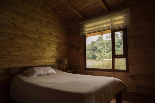 Cama en habitación de madera con ventana en Hermosa Cabaña en La Cocha-Finca INDIANA, en El Encano