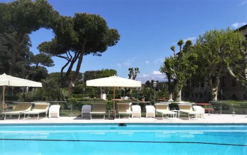 a swimming pool with white chairs and umbrellas at Park Hotel Villa Ariston in Lido di Camaiore