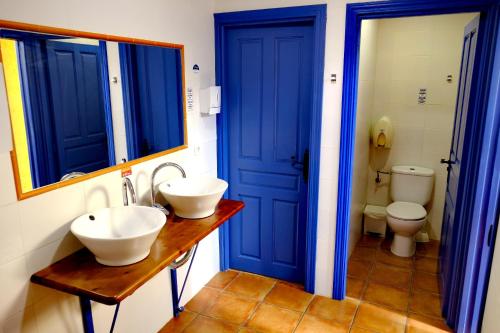 een badkamer met blauwe deuren, 2 wastafels en een toilet bij Albergue San Miguel - Sólo para Peregrinos in Hospital de Órbigo