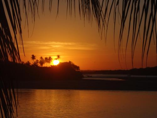 a sunset over a body of water with palm trees at Pousada Água Viva in Ilha de Boipeba