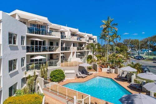 a large apartment building with a swimming pool and umbrellas at Regatta Noosa in Noosaville