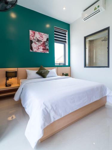 a bedroom with a large white bed with a green wall at Peaceful House Hostel in Dong Hoi