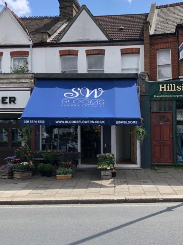 a store with a blue awning on a street at Replingham Road Apartment in London