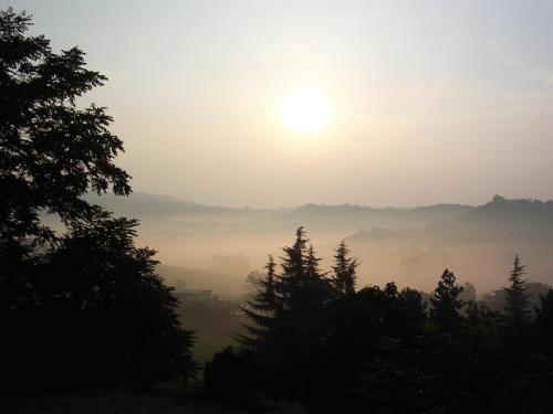 a misty sunrise in the mountains with trees at La Locanda del Melograno in Moncalvo