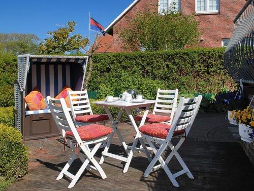 einen weißen Tisch und Stühle mit roten Kissen auf der Terrasse in der Unterkunft Haus Kiebitznuest - Langeoog in Langeoog