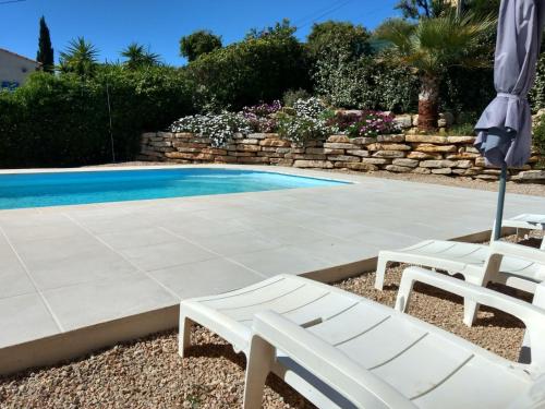 - deux chaises blanches et un parasol à côté de la piscine dans l'établissement Studio Quiétude, à Saint-Aygulf