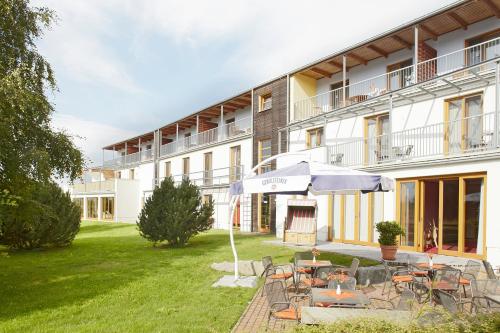 a building with a patio with tables and an umbrella at SEETELHOTEL Nautic Usedom Hotel & Spa das Hotel für Wellness & Genuss auf Usedom in Ostseebad Koserow