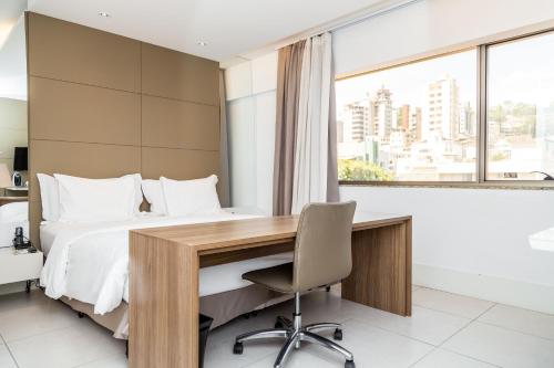 a bedroom with a desk and a bed and a window at Hilton Garden Inn Belo Horizonte Lourdes in Belo Horizonte