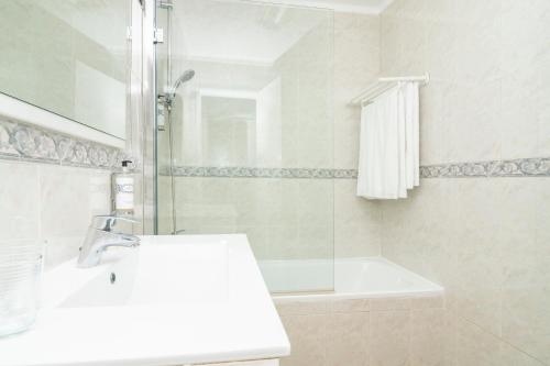 a white bathroom with a sink and a shower at Apartamentos Rossio Mar in Albufeira