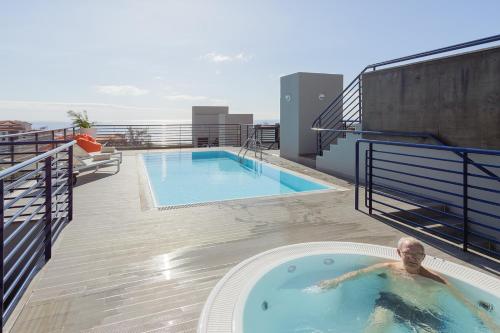 
a man is sitting on the edge of a pool at Terrace Mar Suite Hotel in Funchal
