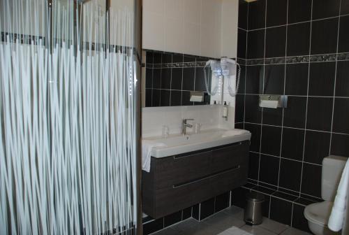 a black tiled bathroom with a sink and a shower at The Originals City, Hôtel Cathédrale, Lisieux (Inter-Hotel) in Lisieux