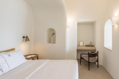 a white bedroom with a bed and a chair at Art Maisons Oia Castle in Oia