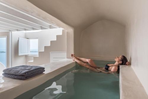 a woman is sitting on the edge of a swimming pool at Art Maisons Oia Castle in Oia