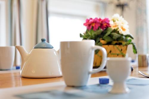 a table with two tea cups and a vase of flowers at Gîtes Les Myosotis in Morhet