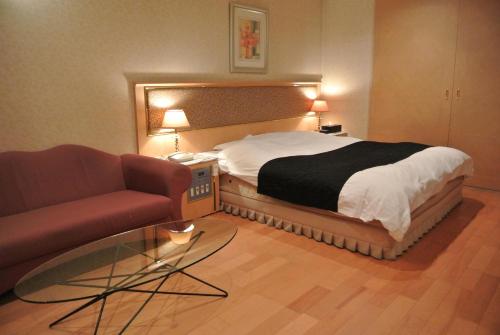ein Schlafzimmer mit einem Bett, einem Sofa und einem Glastisch in der Unterkunft アンジェリーククロッシュ 男塾ホテルグループ in Himeji