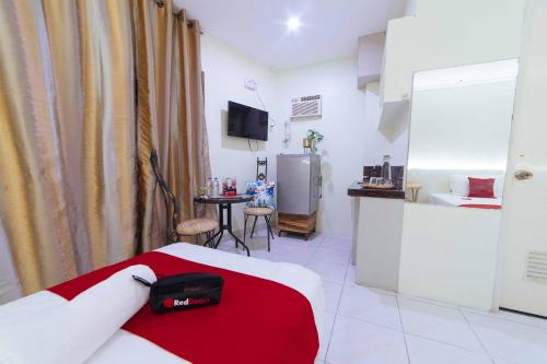 a room with a bed with a red blanket and a kitchen at RedDoorz @ Ledesco Avenue Lapaz Iloilo in Iloilo City