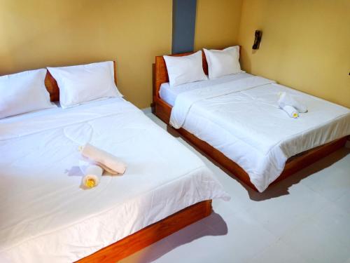 two beds in a room with white sheets and dolls on them at Aryasuta Bungalow in Tetebatu